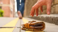 Uma mão se aproxima para pegar uma carteira no chão