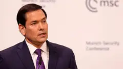 Marco Rubio bir takım elbiseyle küsüde konuşurken arkasında Münih Güvenlik Konferansı logosu görülüyor