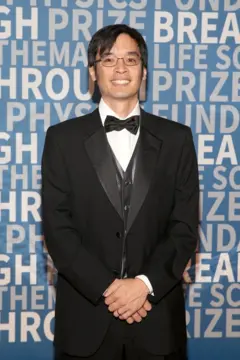 Terence Tao sorri para a câmera. Ele está vestido com um elegante terno preto e gravata borboleta.