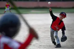 Uma criança de cerca de 5 anos lança a bola para outra, que se prepara para rebater