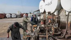 Các công nhân đang sửa chữa một chiếc xe, gần các bồn chứa dầu ở Iraq