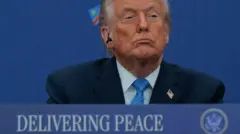 Дональд Трамп за трибуною, на якій написано "Досягаючи миру"