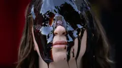 Uma mulher com o rosto coberto por uma substância oleosa.