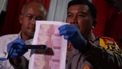 Kapolda Sulawesi Selatan Irjen Pol Yudhiawan (kanan) bersama Kepala Bank Indonesia Perwakilan Sulsel Rizki Ernadi Wimanda (kiri) mengecek barang bukti uang palsu menggunakan detektor mata uang (money detector) saat konferensi pers di Mapolres Kabupaten Gowa, Sulawesi Selatan, Kamis (19/12/2024). Polres Gowa merilis kasus pembuatan dan peredaran uang palsu yang melibatkan oknum pegawai UIN Alauddin Makassar, di kampus dua dengan menyita sebanyak 98 jenis barang bukti termasuk uang palsu pecahan Rp100 ribu sebanyak 4.927 lembar yang sudah terpotong, serta 1.369 lembar kertas bergambar uang pecahan yang sama belum terpotong, kejahatan tersebut diduga melibatkan 17 tersangka sementara tiga terduga pelaku masih DPO. 
