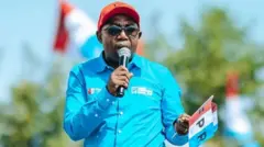 Germain Musonera mw'ishati y'ubururu n'agakofero mu mabara ya FPR afashe n'amabendera ya FPR mu kubamfu, mu kuryo afashe micro