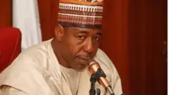 Gomina ipinlẹ Borno, Babagana Zulum. O wọ agbada, o si de fila, ẹrọ gbohun-gbohun wa niwaju rẹ