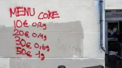 روی دیوار سفید نرخ یک ماده مخدر را با رنگ قرمز نوشته