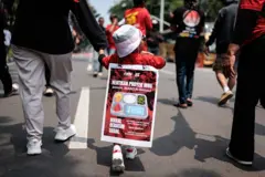 Putri berusia 3 tahun dari anggota Aliansi Gerakan Reforma Agraria (AGRA) ini membentangkan spanduk di punggungnya yang menentang program pangan gratis (MBG)