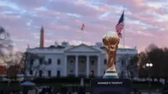 O troféu da Copa do Mundo em frente à Casa Branca, ao lado de bandeiras dos Estados Unidos e com o Monumento a Washington ao fundo