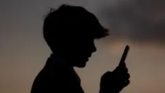 Профиль 13-летнего подростка, который смотрит в экран смартфона