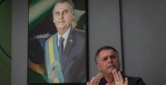 Jair Bolsonaro aparece sentado com um retrato de si mesmo ao fundo