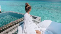 Mulher vestida de branco, olhando para o oceano.