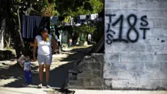 Mujer y niño junto a un grafiti del Barrio 18 en la colonia Valle del Sol en Apopa, El Salvador. (Foto: José Cabezas / Getty Images)