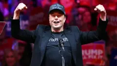 Elon Musk, vestido de negro, eleva sus brazos en señal de triunfo durante un acto político de Trump en octubre 