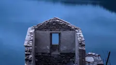 Paredes de una casa en ruinas, por una ventana se ve el lago azul