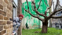 Carlos Serrano ao lado do mural de Banksy em Finsbury Park, Londres