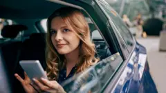 žena u automobilu drži telefon u ruci