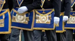 Процессия масонов. На фотографии изображены мужчины от пояса вверх, одетые в белые перчатки и носящие герб масонов, вышитый золотой нитью на королевском синем фоне.