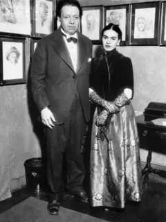Diego Rivera posa em pé ao lado de Frida Kahlo. Ele usa terno preto e gravata-borboleta, e ela veste um longo vestido cuja parte superior é preta e cuja parte inferior, aparentemente de seda, é de cor mais clara. Também usa luvas que cobrem os braços. Atrás deles há vários quadros com rostos pintados
