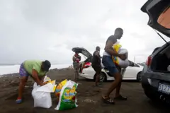 Varias personas cargan costales de arena a sus vehículos en una playa de Jamaica