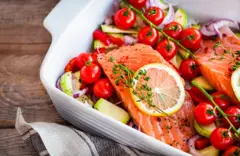Un salmón en una bandeja con tomates, hierbas y otras verduras, antes de ser horneado