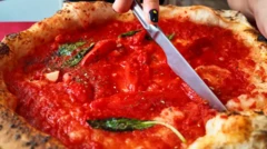 Mão feminina cortando uma pizza cheia de molho de tomate com faca