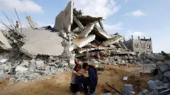 فتيات يجلسن أمام مبان مدمرة في غزة.
