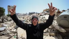 Una mujer libanesa de mediana edad, con vestidura islámica negra, hace la señal de la paz con dos manos en alto, frente a los escombros causados por los ataques israelíes en la ciudad de Tiro