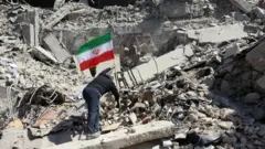 رجل إيراني يضع العلم الإيراني بين أنقاض مبنى مركز شرطة متضرر في وسط مدينة طهران