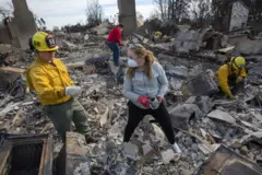 Bombeiros ajudam uma mulher a examinar os restos de sua casa destruída pelo incêndio na área de Pacific Palisades, em Los Angeles, Califórnia, nos Estados Unidos, em 22 de janeiro de 2025