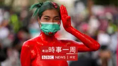 泰國曼谷收押監獄外一名全身潑上紅色油漆的女示威者舉起《饑餓遊戲》三指抗議手勢（13/10/2021）