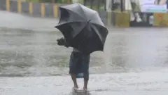A man with an umbrella wades through floodwater in Khulna, Bangladesh