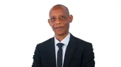 Ifoto ngufi igaragaza Profeseri Emile Bienvenu yambaye ikositimu y'umukara, ishati y'umweru na karuvati y'umukara. Arareba muri 'camera'. 