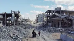 صورة التقطتها طائرة بدون طيار تُظهر أشخاصًا يسيرون عبر حي سكني مدمر، بعد انسحاب القوات الإسرائيلية من المنطقة، وسط وقف إطلاق النار بين إسرائيل وحماس في غزة، في مدينة غزة، 18 أكتوبر/تشرين الأول 2025. 