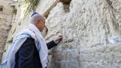 رئيس الوزراء الإسرائيلي، بنيامين نتنياهو، أمام الحائط الغربي (حائط البراق) في القدس في 12 يونيو/حزيران 2025، يضع ورقة  مكتوب عليها آية من الكتاب المقدس "هو ذا شعب يقوم كلبؤة، ويرتفع كأسد" (سفر العدد 24:23)
