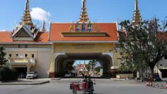 国境紛争の影響で閉鎖中の検問所の前の道路に、オートバイとそれにつながったリヤカーのようなものに乗った人がいる。検問所は屋根に塔がついている大型で装飾が施された施設で、下部がトンネル状態になっている