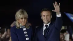 French President Emmanuel Macron waves on stage next to his wife, French first lady Brigitte Macron, after being re-elected as president, following the results in the second round of the 2022 French presidential election, during his victory rally at the Champ de Mars in Paris, France, April 24, 2022.