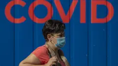 A woman wearing protective face mask walks in front of a coronavirus testing station