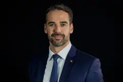 Eduardo Leite sorri para a foto. Ele usa um terno azul, camisa branca e gravata azul.