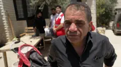 Rafeeq Abu Alia, residente en al Mughayyir, con camisa negra y un cochecito de bebe al lado. Al fondo se ven tres hombres desenfocados.