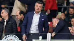 Sadettin Saran Konyaspor tribününde Fenerbahçe maçını izlemek için yerini alırken, üstünde lacivert bir ceket ve açık renkli bir gömlek var