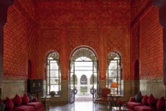 Una gran sala con paredes rojas elaboradamente talladas, muebles de color rojo oscuro y una gran puerta que da al patio.