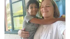 Katrin sorri para a câmera com um bebê nos braços no Hospital Nasser, em Gaza.