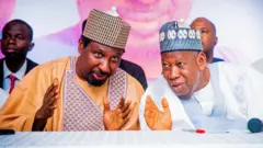 Sanata Barau Jibril da tsohon shugaban APC, Abdullahi Ganduje suna zantawa a wani taro, inda suka ɗaga hannayensu