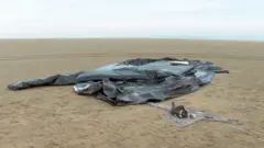 Les restes d'un bateau pneumatique sont abandonnés sur une plage du nord de la France. Une grande quantité de ce qui ressemble à une bâche en plastique noir est pliée au hasard sur une grande étendue de sable plat.