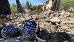 Some crockery is displayed near a home that has been reduced to rubble