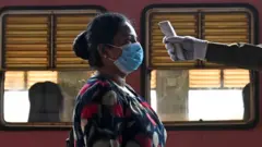 A guard checks the temperature of a government employee as she returns to work after a 52-day lockdown which was imposed as a preventive measure against the COVID-19 coronavirus, in Panadura a suburb of the Sri Lanka's capital Colombo on May 11, 2020. - Sri Lanka will partially reopen from May 11, ending a 52-day lockdown as the community spread of the coronavirus had been brought under control, the health minister said.