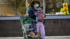 A mother wearing a face mask to protect against the coronavirus disease and her babies wait for a bus in central Moscow on September 30, 2020.