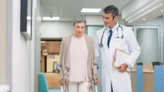 Una mujer con una fractura trata de caminar con muletas junto a un médico.
