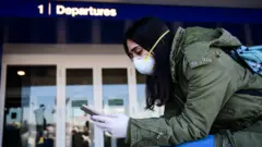 A passenger wearing a protective face mask looks her phone in Linate Airport in Milan